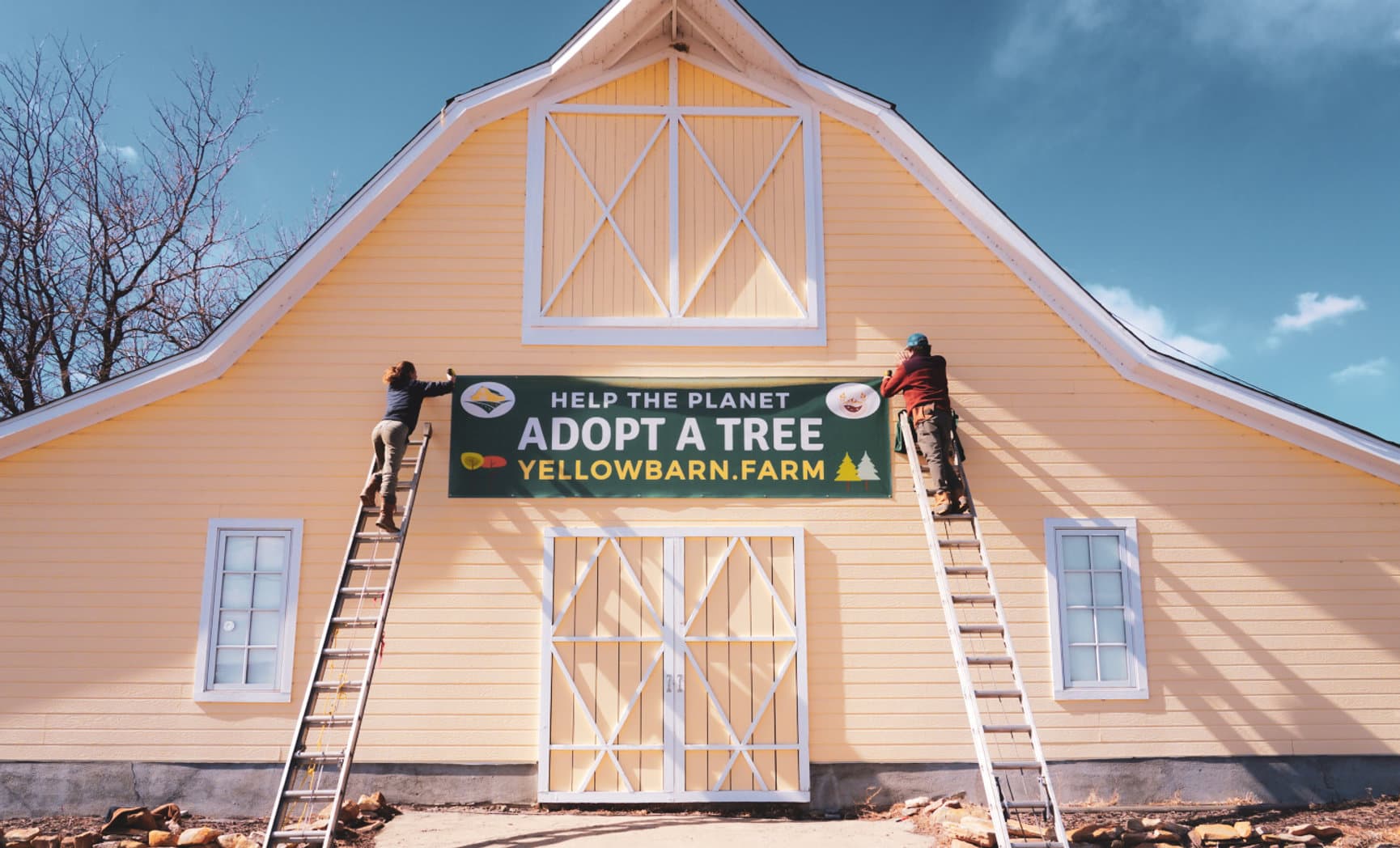 Yellow Barn Farm with a HELP THE PLANET — ADOPT A TREE banner across the barn
